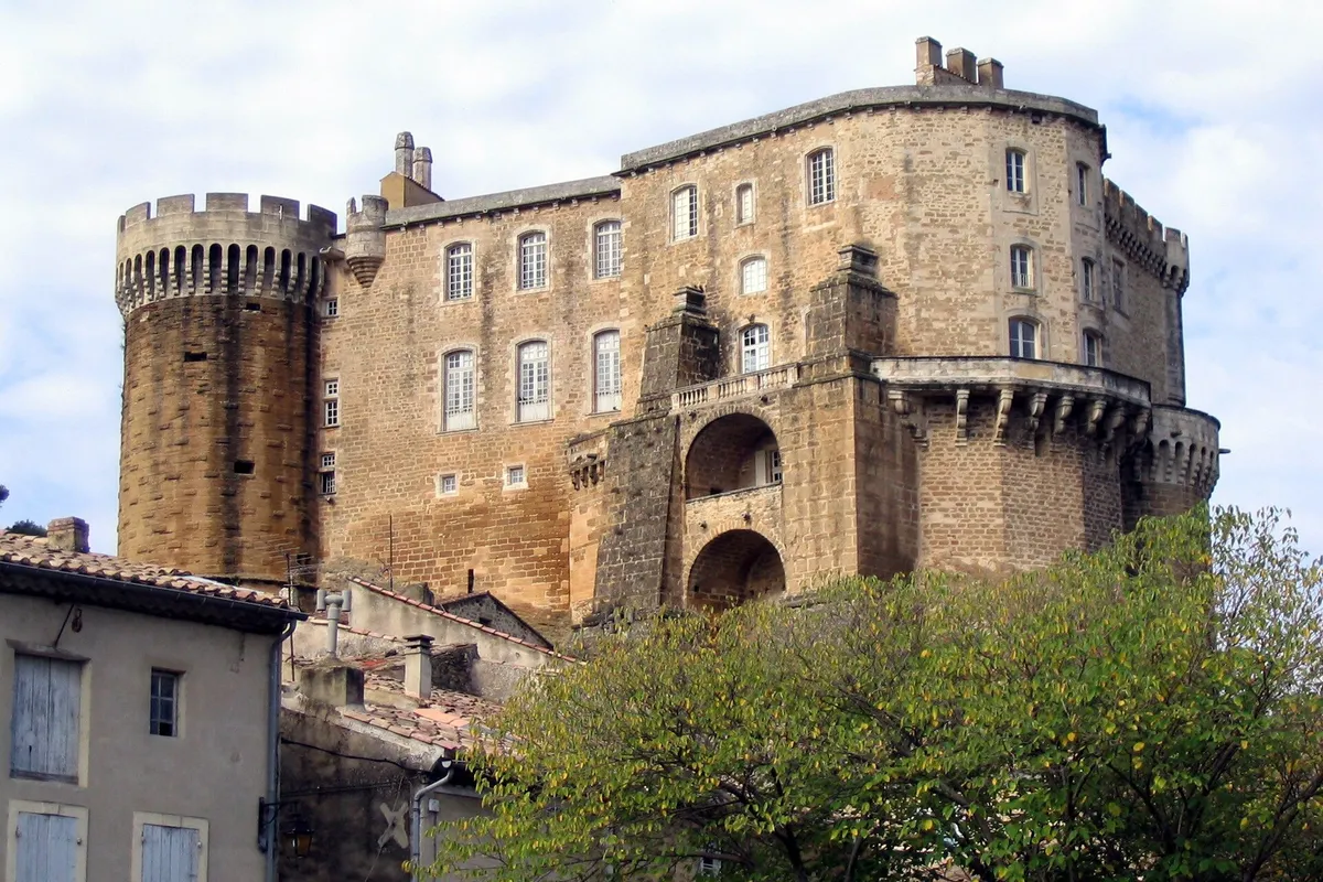 Le château de Suze-la-Rousse, avec sa tour ronde crénelée et sa haute façade de pierre dorée